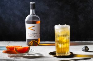 A bottle of whisky with a highball glass of whisky and tonic and a small bowl of orange slices