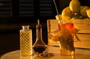 A cocktail on a table with jars and a box of lemons