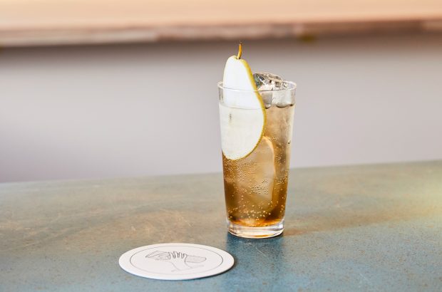 A drink on a bar counter garnished with a slice of pear