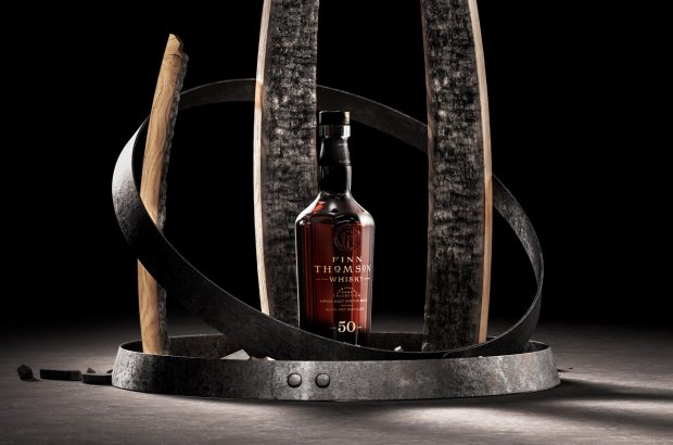 A bottle of whisky standing between staves of wood against a black background