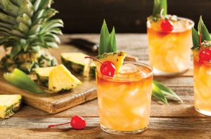 Three cocktails on a wooden bar with pineapples