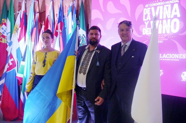 Three people stand next to a Ukrainian flag at a conference