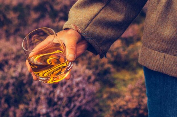 Hand holding glass of whisky in outdoor setting