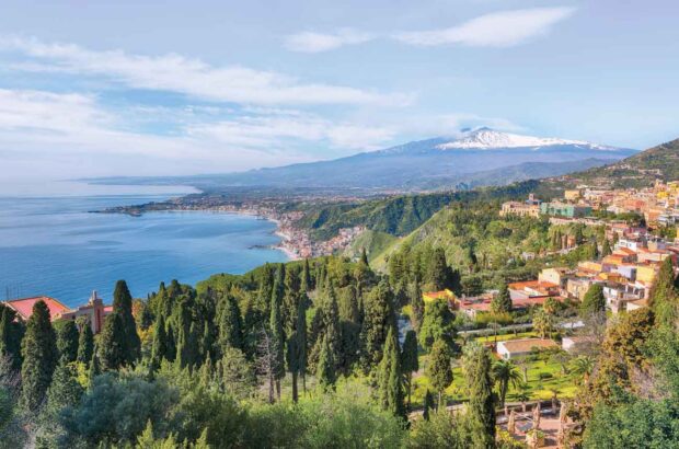 The hilltop town of Taormina overlooking Giardini Naxos bay, facing snow-capped Mount Etna.