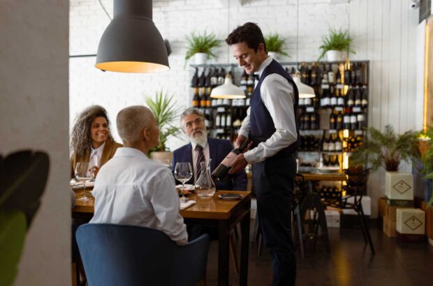 Image of sommelier presenting wine to guests at a restaurant.