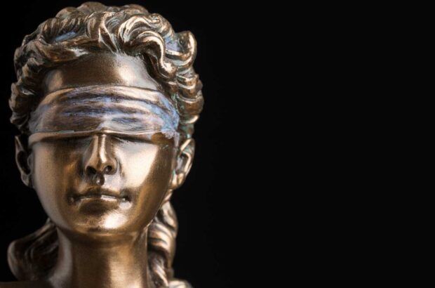 Image of the blindfolded goddess of justice Themis isolated on black background.