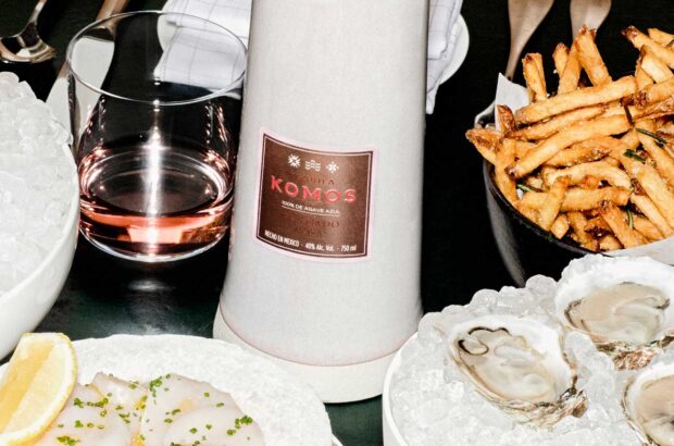 Bottle of Komos rosa tequila on table with oysters and fries