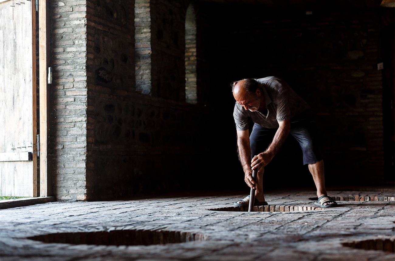 Qvevri are buried underground to maintain a constant temperature. The winemaker is punching down the cap to encourage extraction.