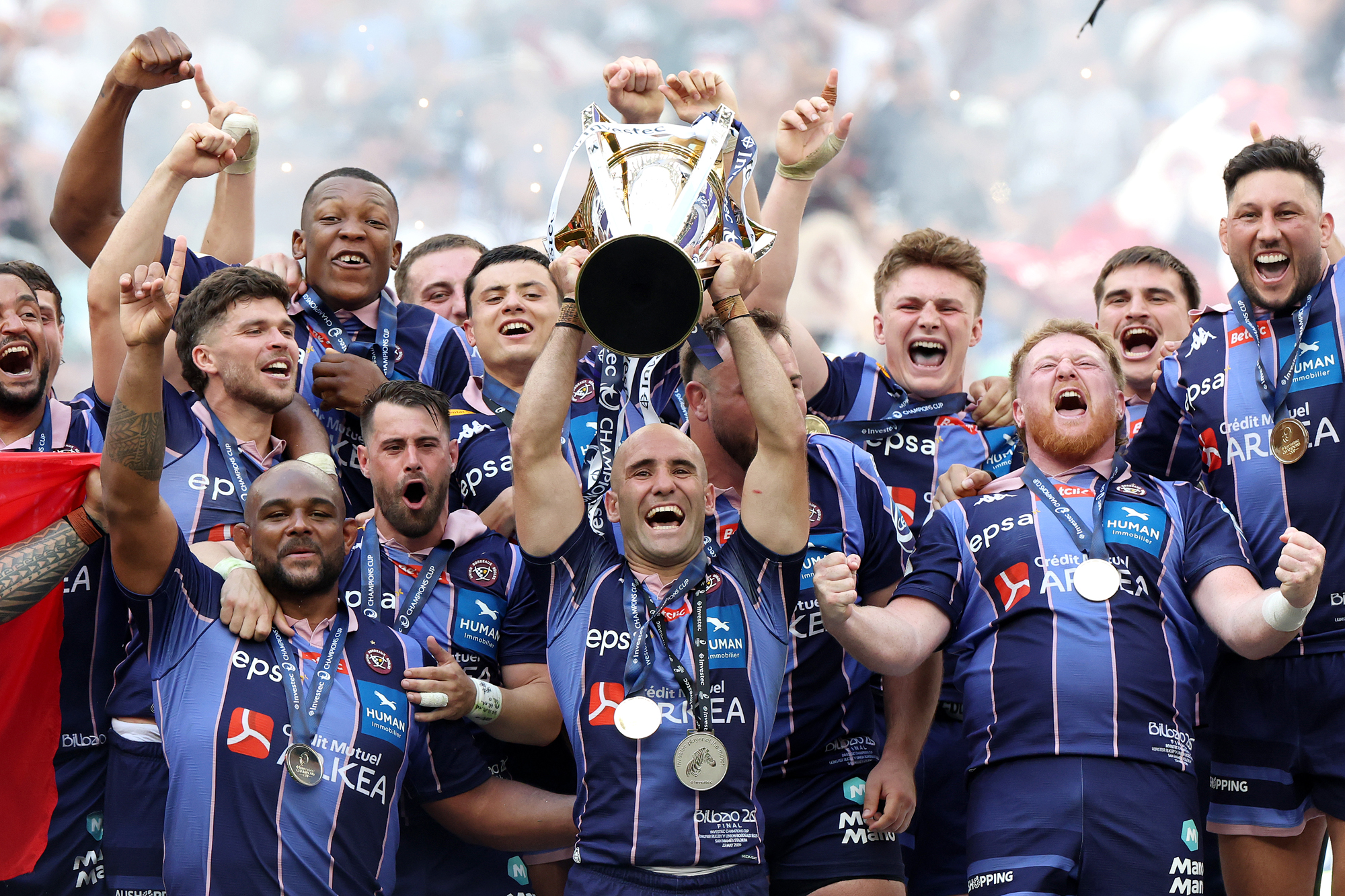 Bordeau Bègles captain Maxime Lucu holds the European Champions Cup aloft surrounded by teammates following the team's 2026 victory over Leinster