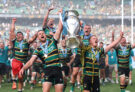 Rory Hutchinson and Fin Smith lift the Gallagher PREM trophy in front of other Northampton Saints players after their 2026 play-off final victory