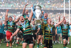 Rory Hutchinson and Fin Smith lift the Gallagher PREM trophy in front of other Northampton Saints players after their 2026 play-off final victory
